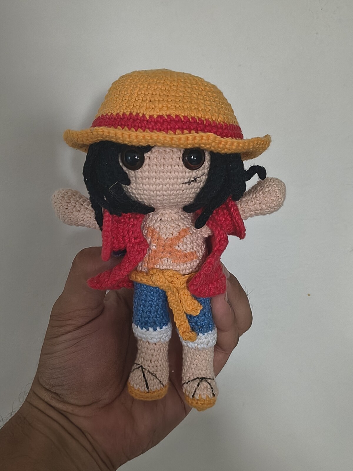 The finished Monkey D. Luffy amigurumi held in a hand, showing the straw hat, red vest, yellow sash and blue shorts