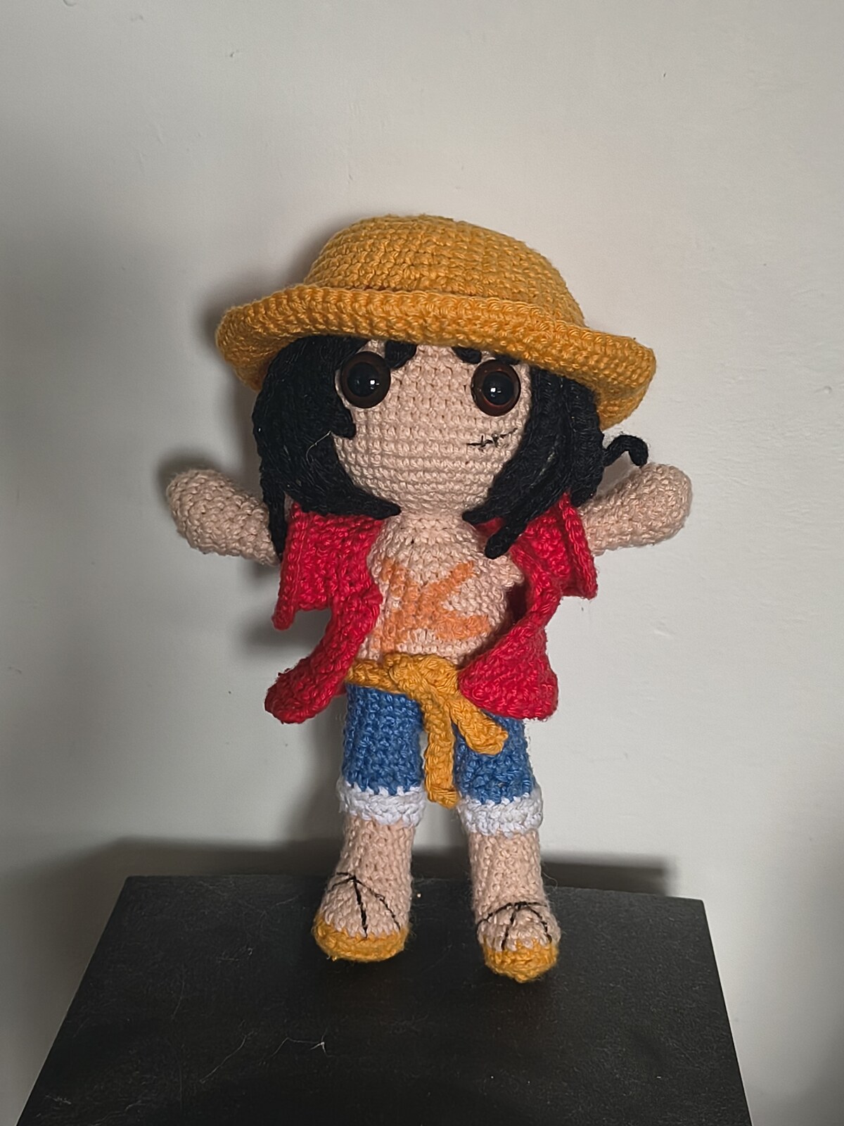 The finished Monkey D. Luffy amigurumi standing on a black stand, arms out