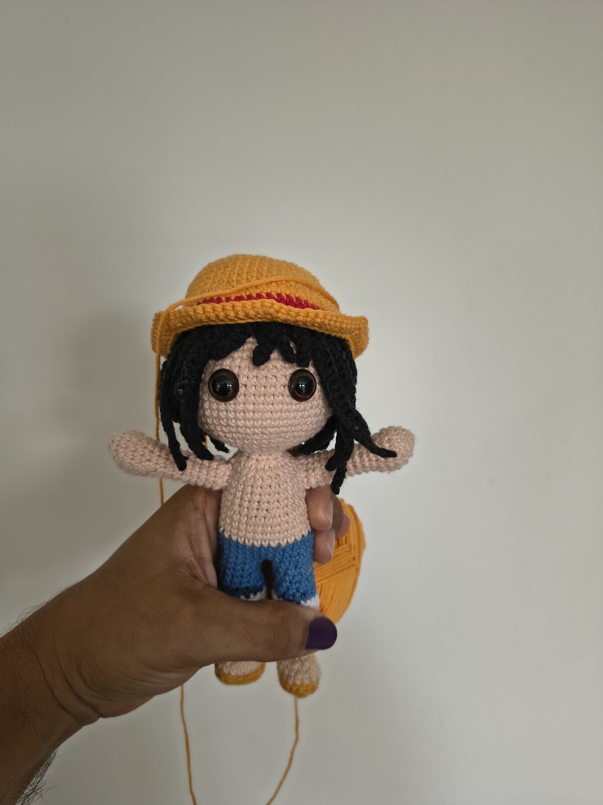 Work in progress: the amigurumi with black yarn hair, safety eyes and arms attached, wearing the straw hat but no vest