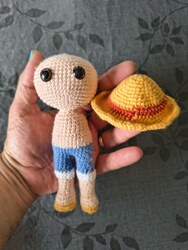 Work in progress: a bare amigurumi body in skin-coloured yarn with blue shorts, held next to the finished straw hat