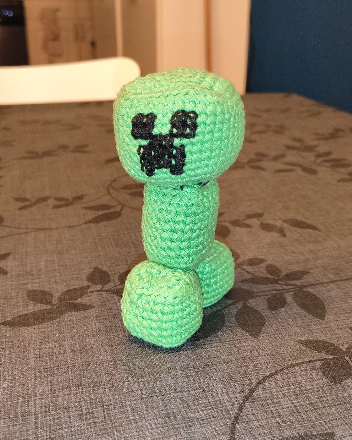 The finished Minecraft Creeper amigurumi, standing on the kitchen table, facing the camera