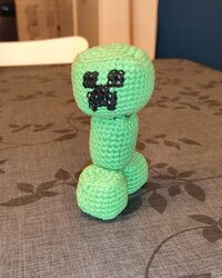 The finished crochet Minecraft Creeper, standing on a table and facing the camera